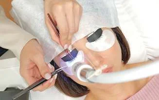 A lash artist setting extensions under an LED light